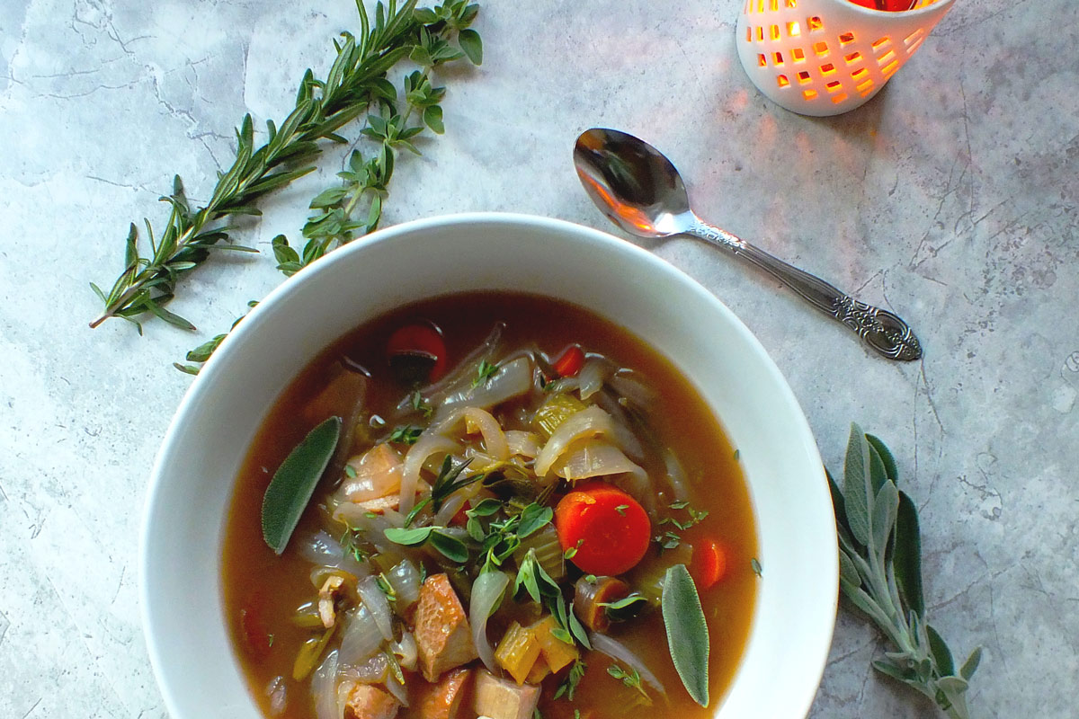 Turkey, vegetables, aromatics, and herbs sit in a rich brown broth in a white bowl.