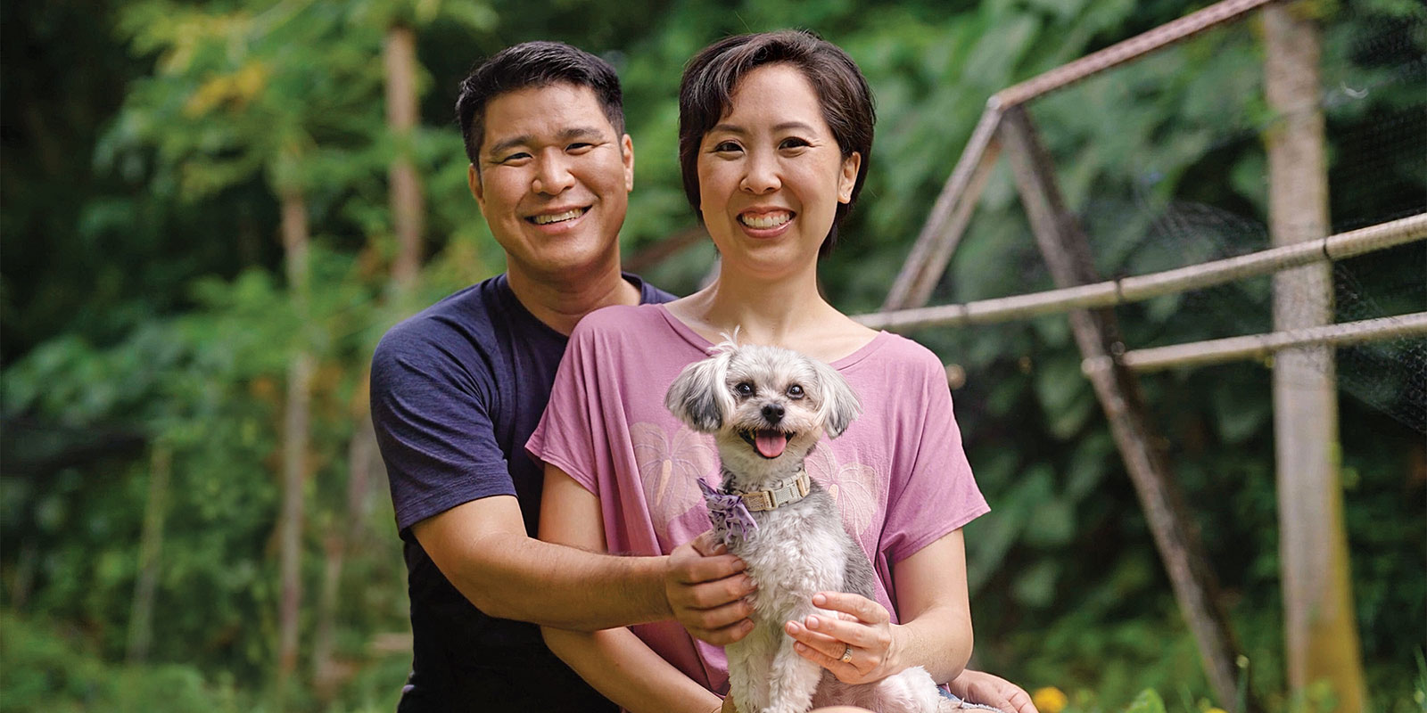 Woman in pink shirt holding and adorable doc with a pink collar alongside her husband.
