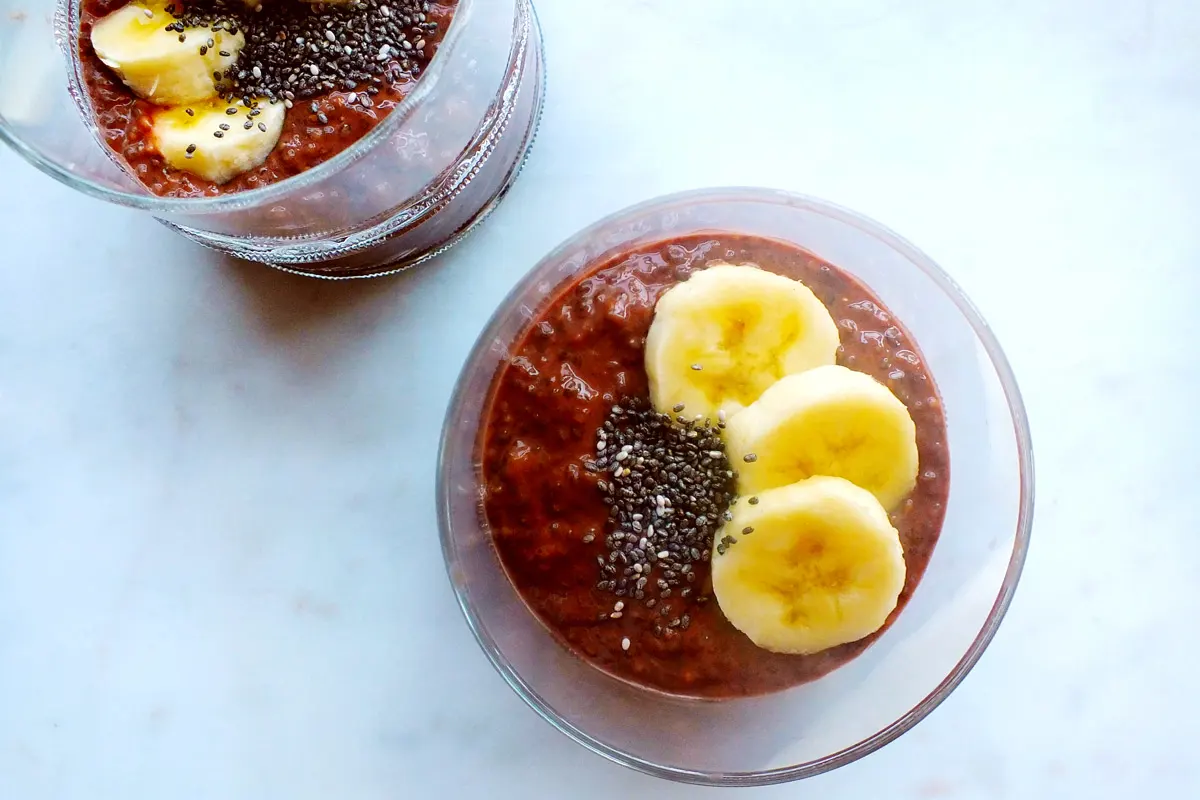 Two servings of pudding in clear glasses with chia and banana garnish.