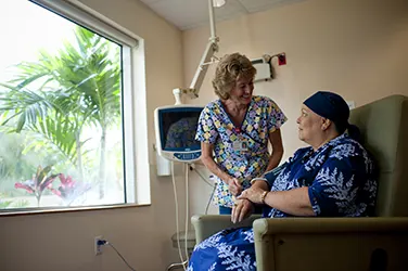 Health care worker smiling at a cancer patient sitting in a chair.