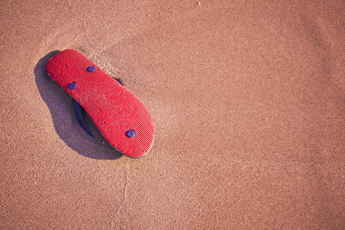 red rubber slipper upside down on top of some moist beach sand