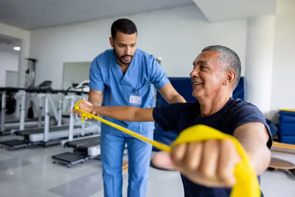 a male physical therapist helps a male patient with stretch band exercises