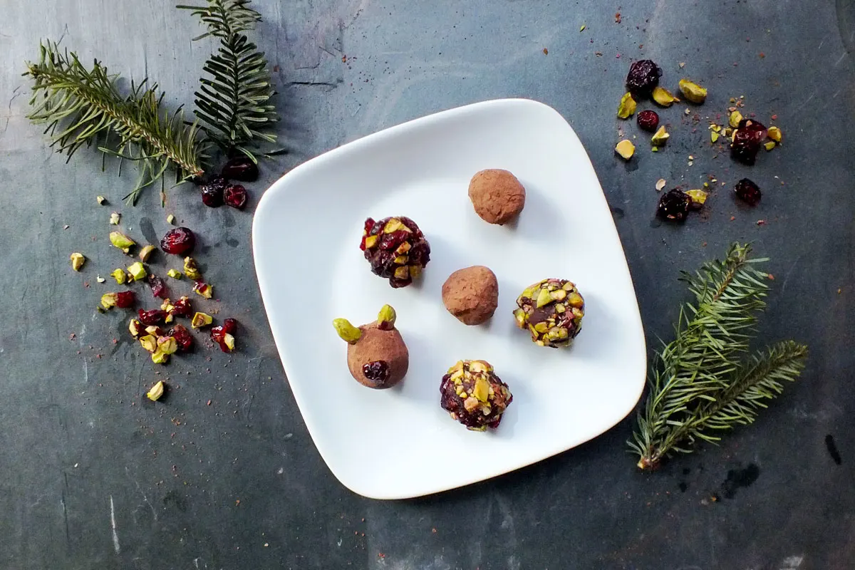 Cookies with various decoration arranged on a white plate with evergreen and toppings in the background.