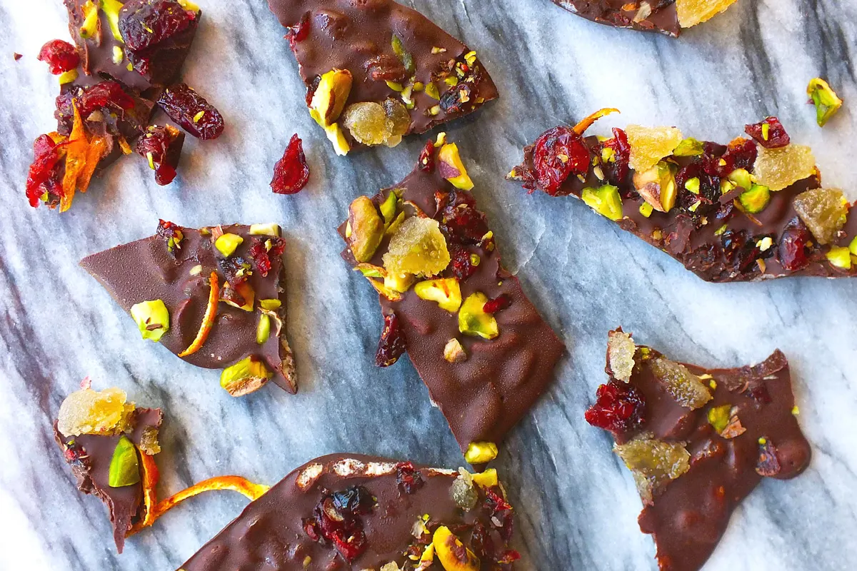 Colorful holiday bark with candied orange, cranberry and green pistachios sit on a marble background