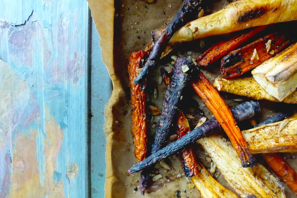 Roasted purple, orange, and white carrots covered in spices sit on a bakng tray
