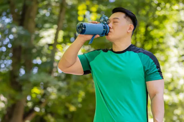 an athletic man drinks water from a reusable water while outdoors
