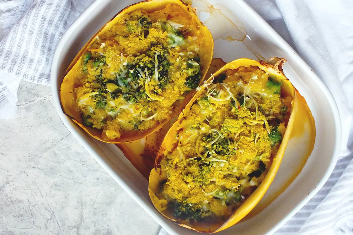 Two halves of spaghetti squash filled with greens and cheese sit in a baking dish.