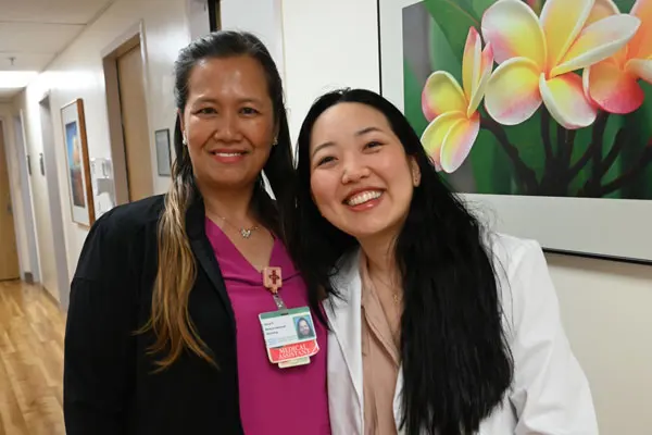 two female health care providers standing in a clinic hallway and smiling at the camera 