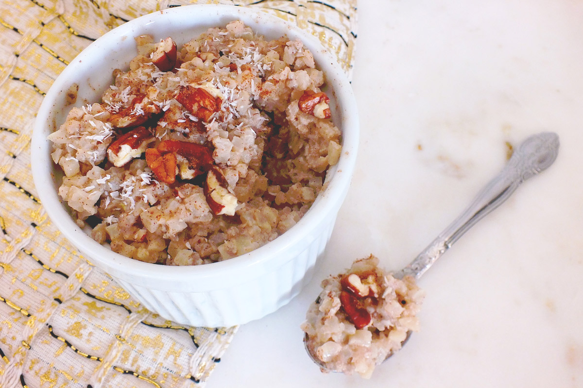 Bowl of Coconut Cauliflower "Rice" Pudding with a spoonful of pudding sitting next to the bowl.