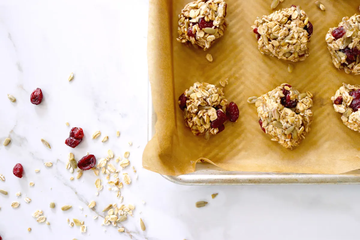 Loose oats and cranberries sit next to a tray of breakfast cookies that are ready to bake.