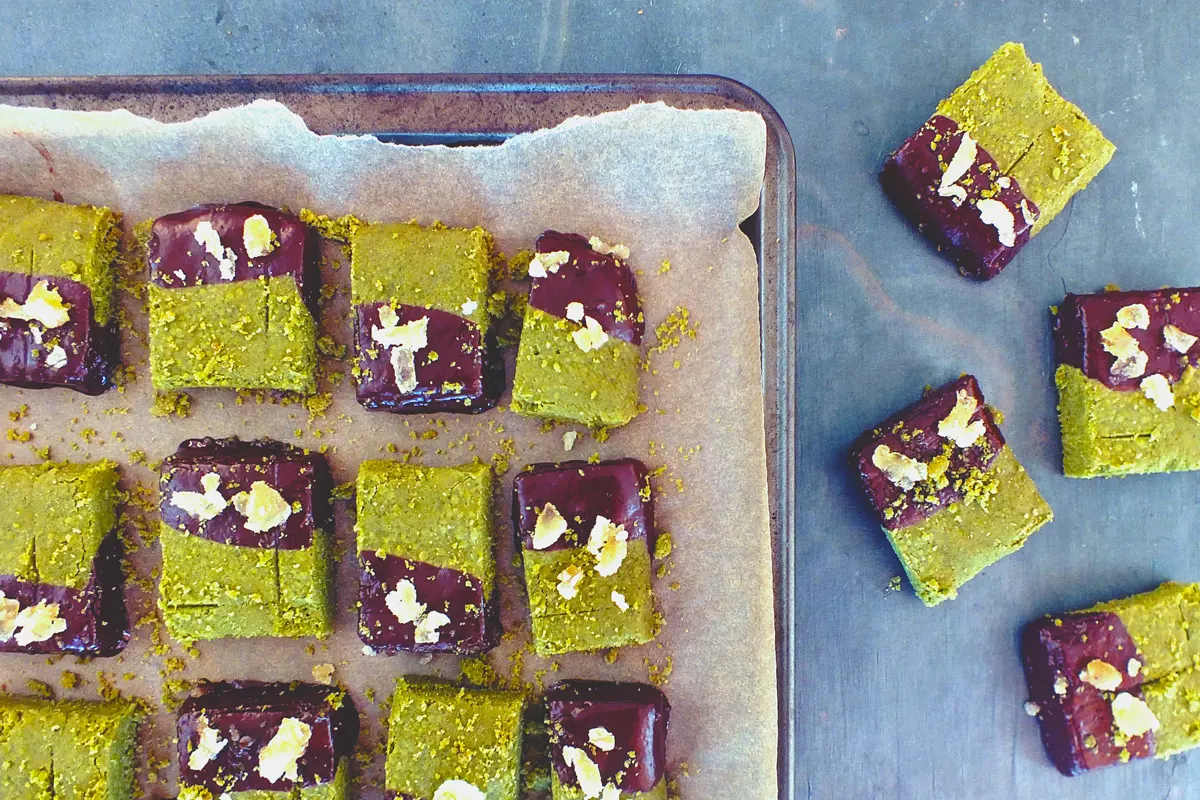 Finished shortbreads, light green and chocolate brown, sit on a baking tray.