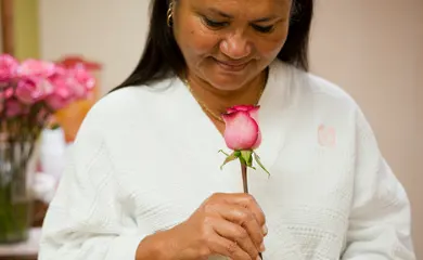 Woman in robe looks at a rose in her hand.