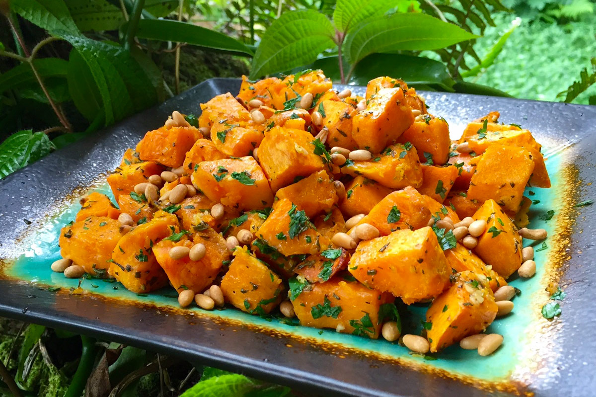 Cubes of orange sweet potatoes sit on a decorative plate with a background of greenery