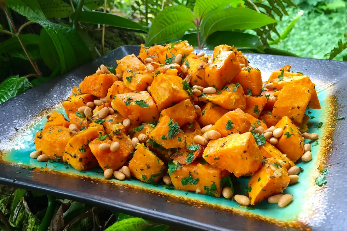 Cubes of orange sweet potatoes sit on a decorative plate with a background of greenery