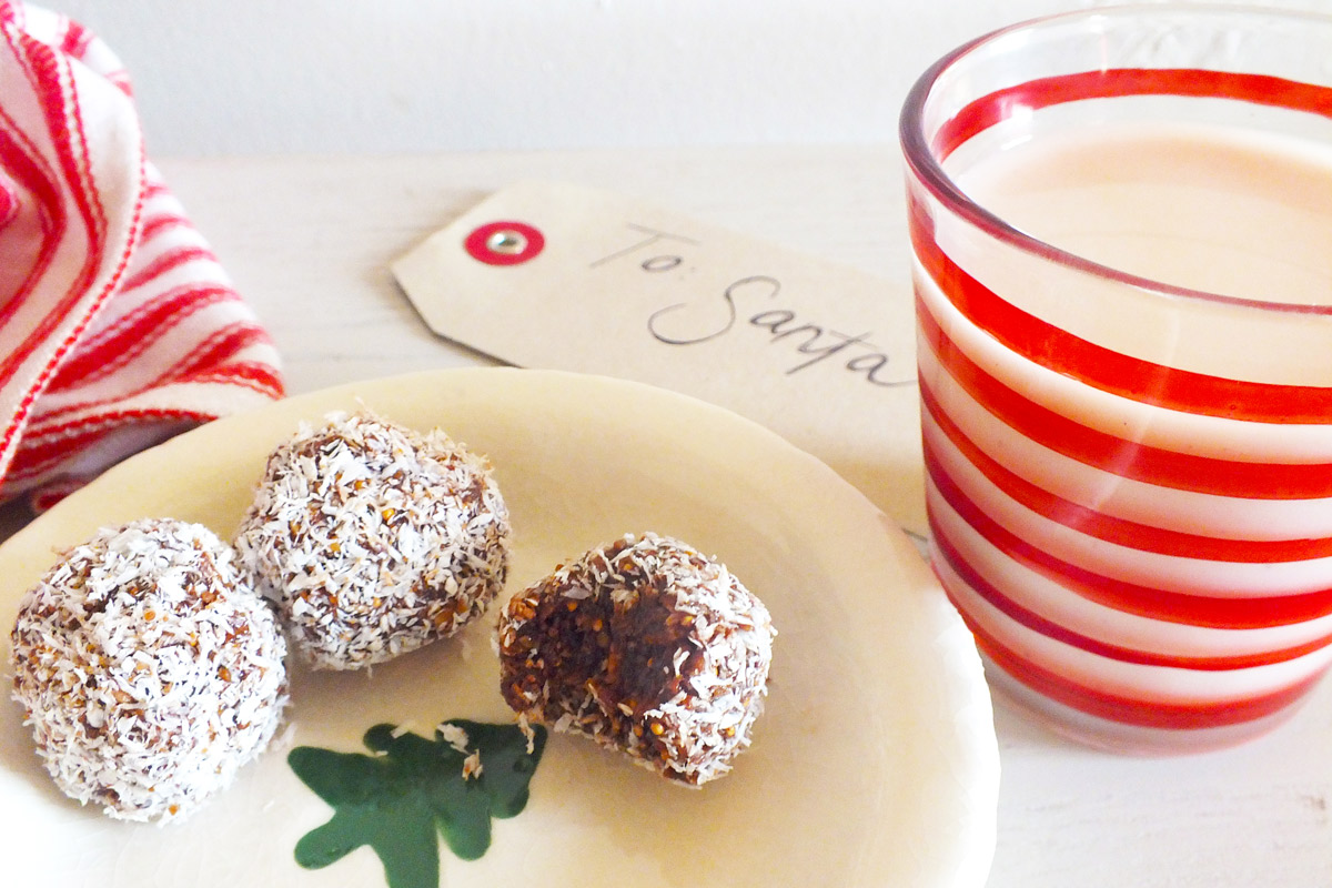 Coconut-covered sugarplums arranged on a plate next to a glass of milk and a tag saying "To Santa"