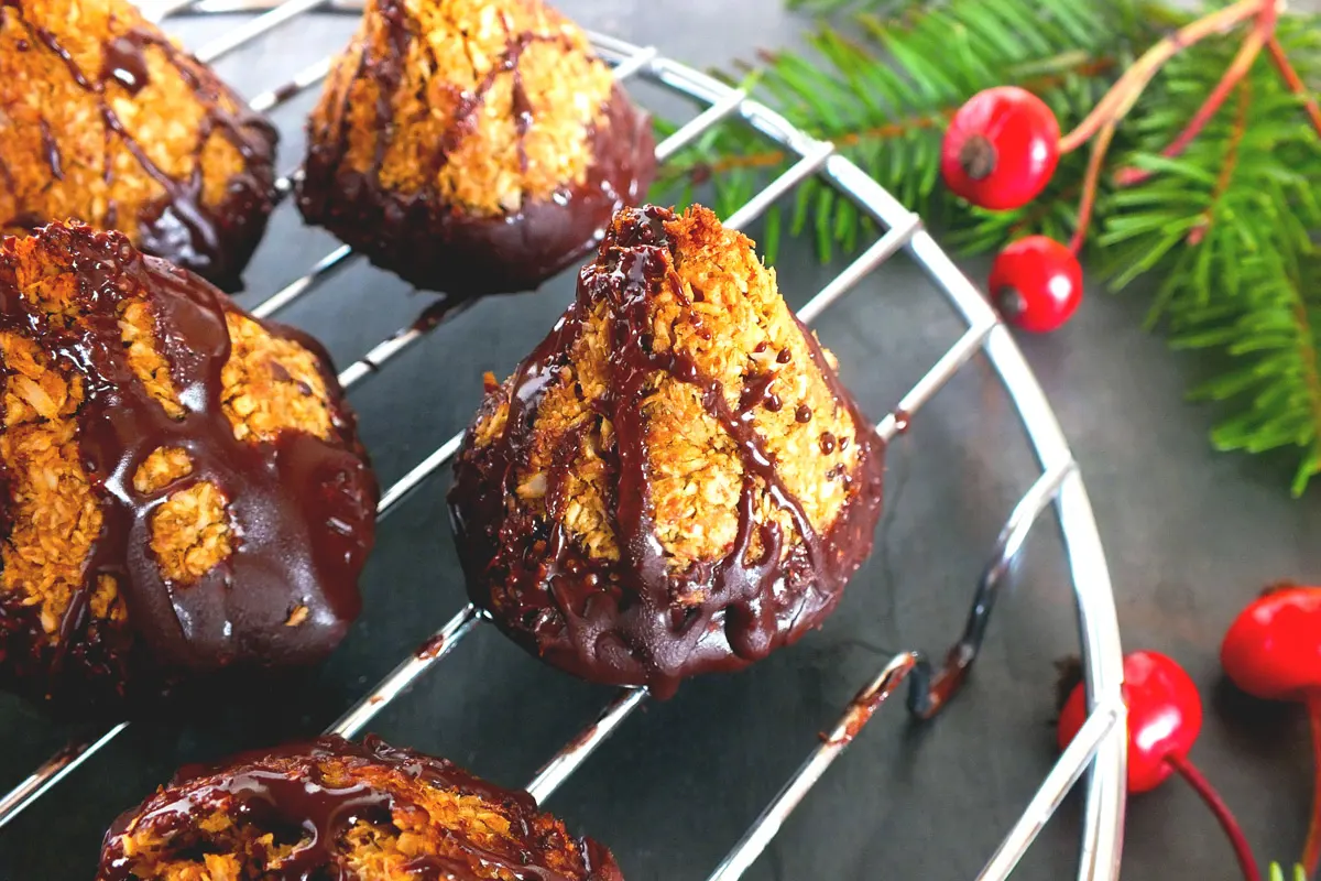A close up of the chocolate-dipped macaroons with some red and green holiday foliage in the background.