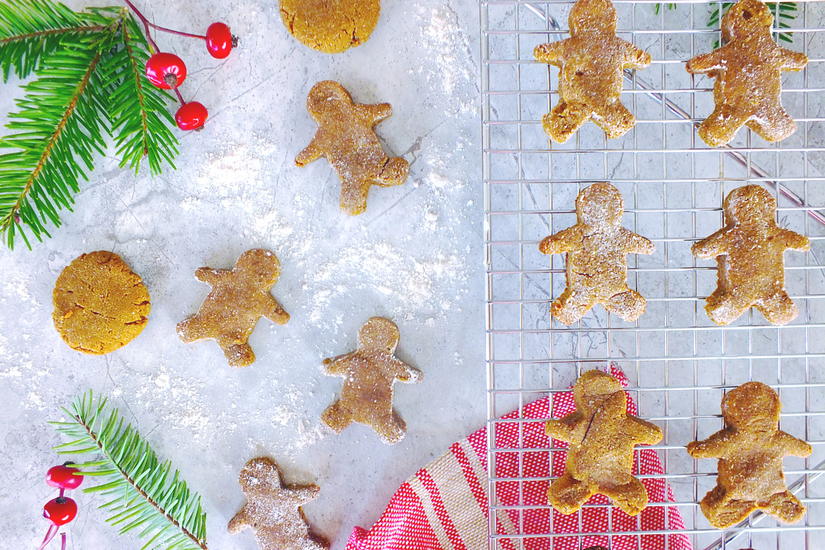 Gingerbread cookies dusted with flour on a cooling rack with holiday berries in the background.