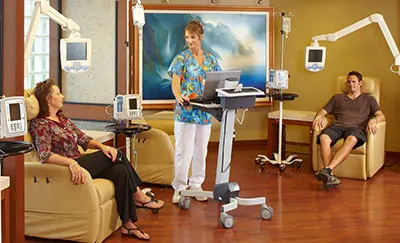 Health care worker standing and talking with patients sitting in chairs.