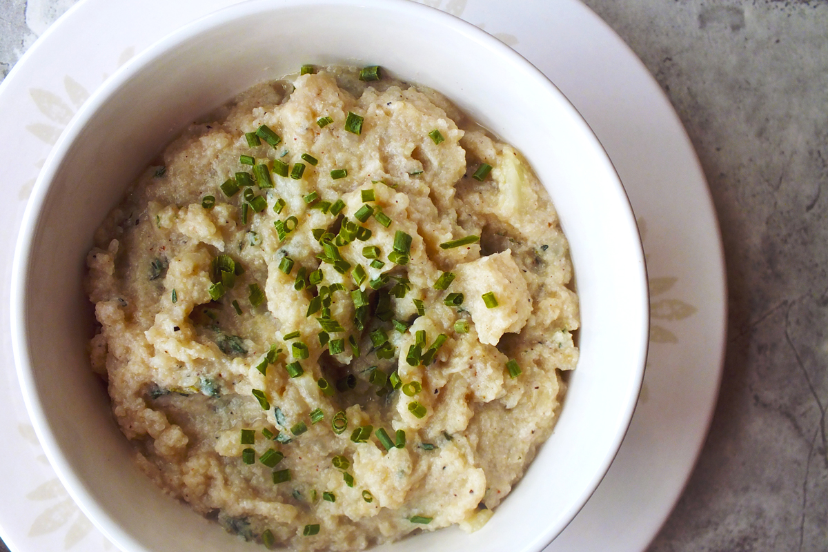 Mashed cauliflower with chive garnish in a white bowl.