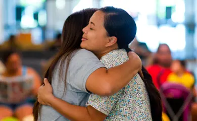 Two women hug in front of a group.