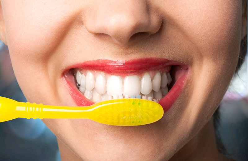 A close up of a lady smiling and brushing her teeth.