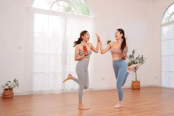 two young women dressed in workout wear give a high-five in a yoga studio