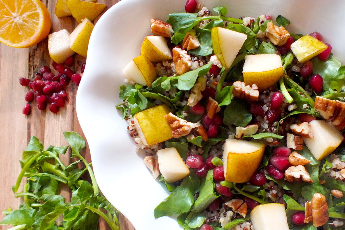 Pears, walnuts and pomegranate seeds sit on quinoa and watercress in a while bowl.
