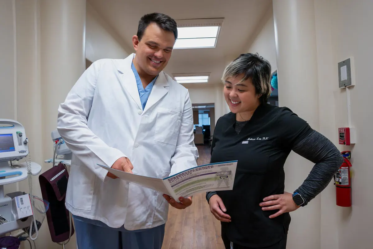A doctor and nurse look over a brochure in a hallway.