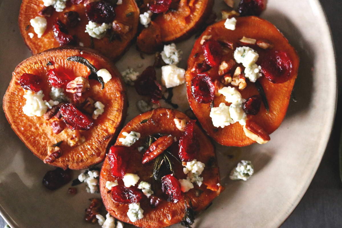 A plate of sliced sweet potato rounds topped with crumbled blue cheese, chopped pecans and dried cranberries.