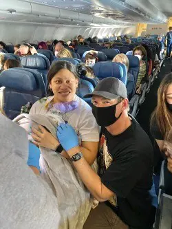 Masked doctor and mom holding newborn baby on airplane.